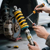Mechanic working on car suspension, highlighting consequences of driving with worn-out shocks consequences.